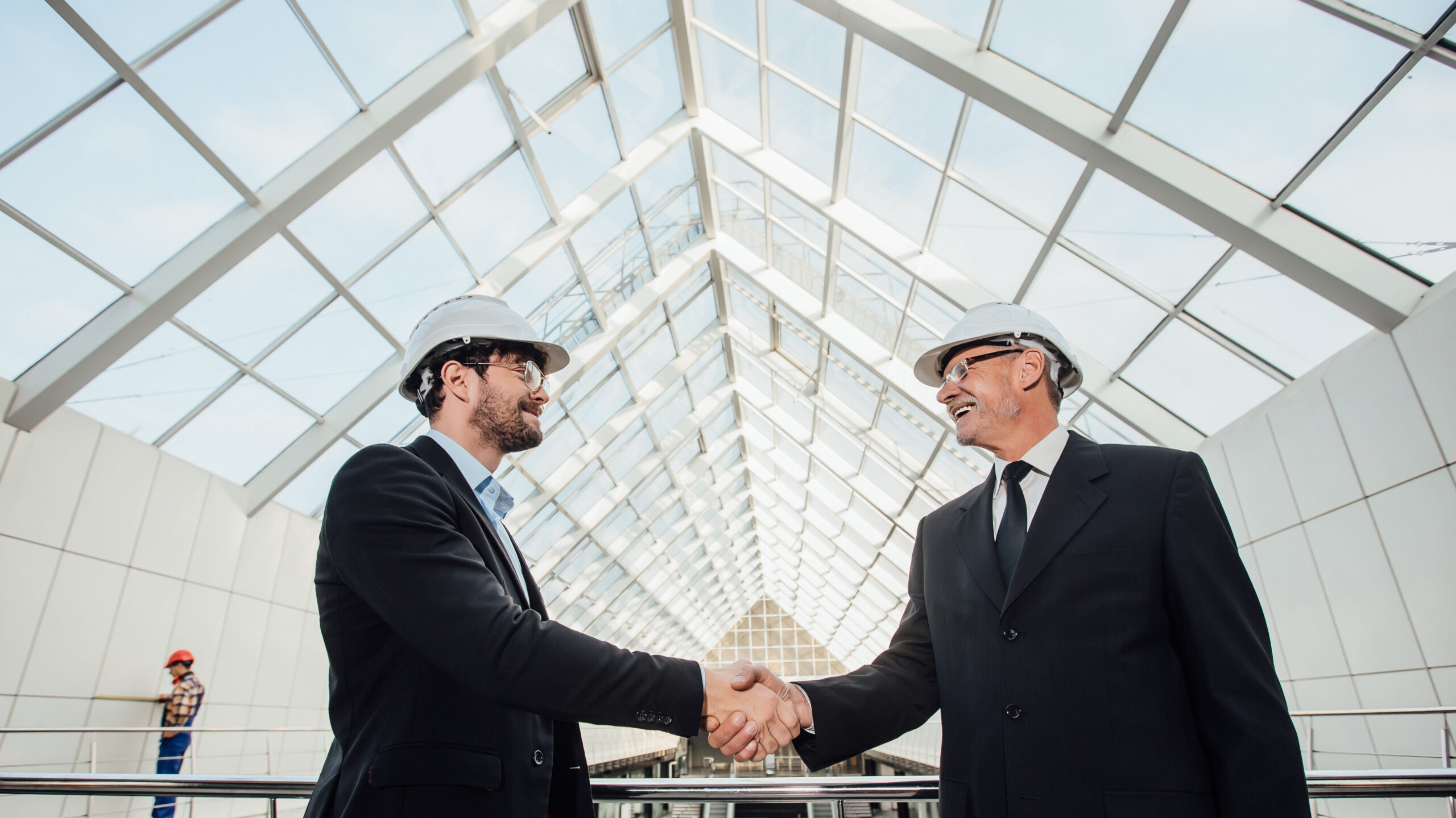 two cheerful businessman handshaking in helmet at new building.